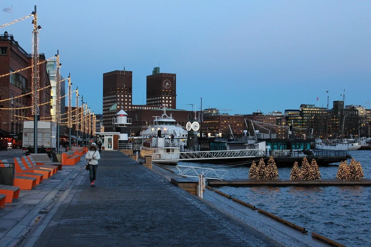 Nabrzeże Aker Brygge o zmierzchu, w tle wieże ratusza, Oslo